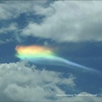 A photo of a rainbow shimmering behind a cloud