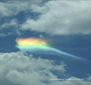 A photo of a rainbow shimmering behind a cloud
